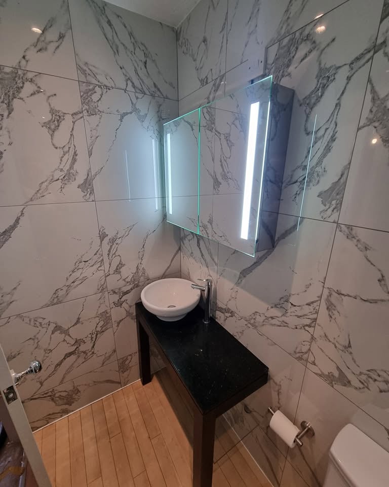 Marble-tiled bathroom with vanity basin and illuminated mirror by Clayton Plumbing and Maintenance