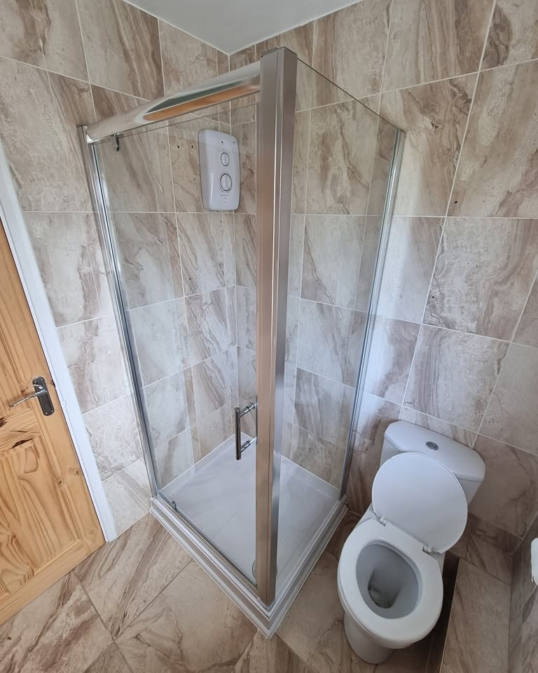 Completed shower cubicle with chrome frame in the same marble-tiled bathroom